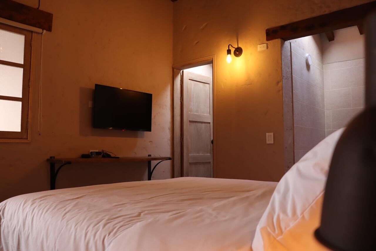 A bedroom with a bed, a television mounted on the wall, and a door leading to another room.