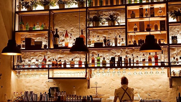 A bar with shelves of bottles and glasses, a bartender, and a rustic stone wall. - Valerio Hotel Boutique  (Marinilla)