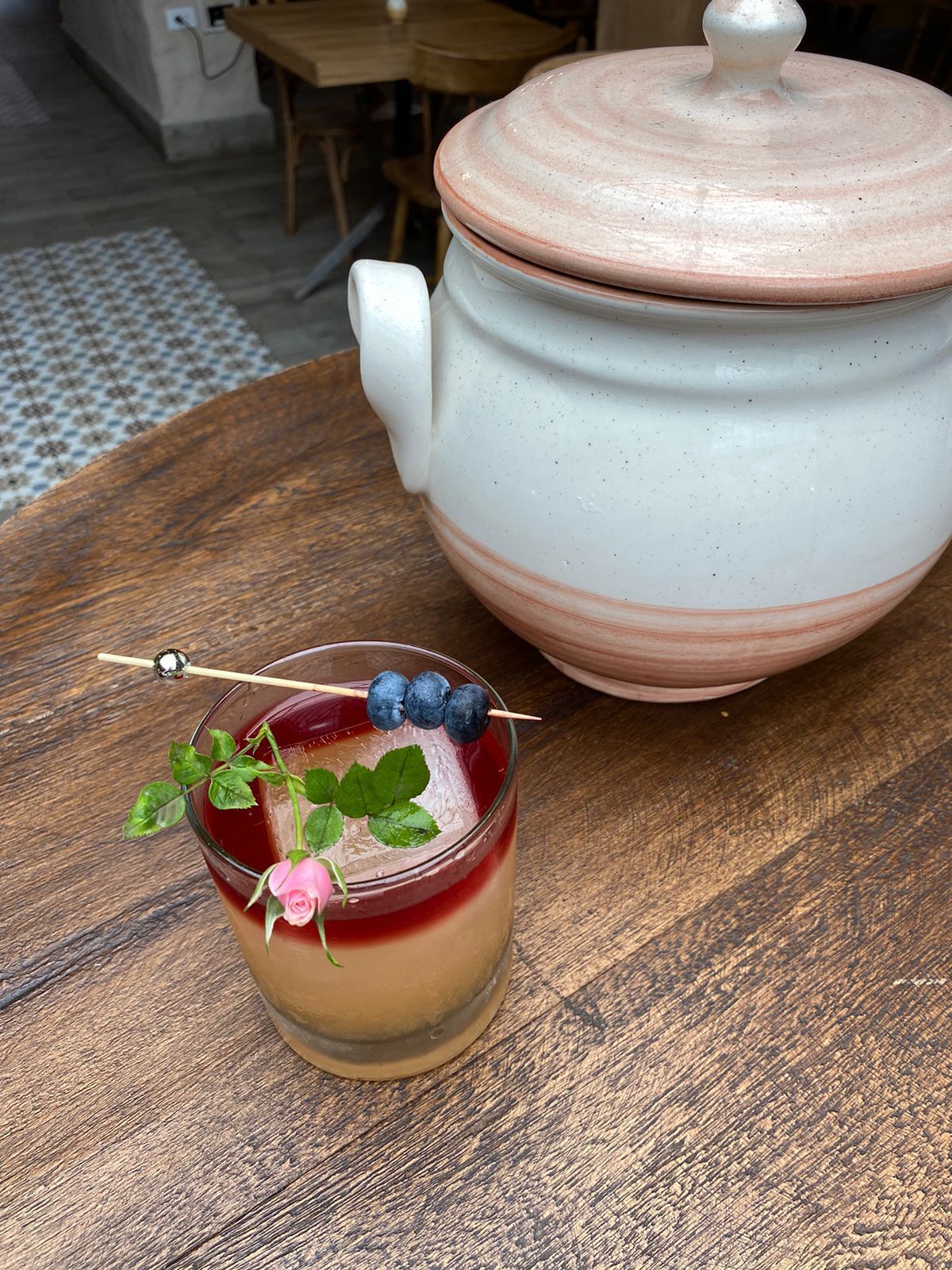 A glass of iced beverage with a rose and blueberries on a wooden table.