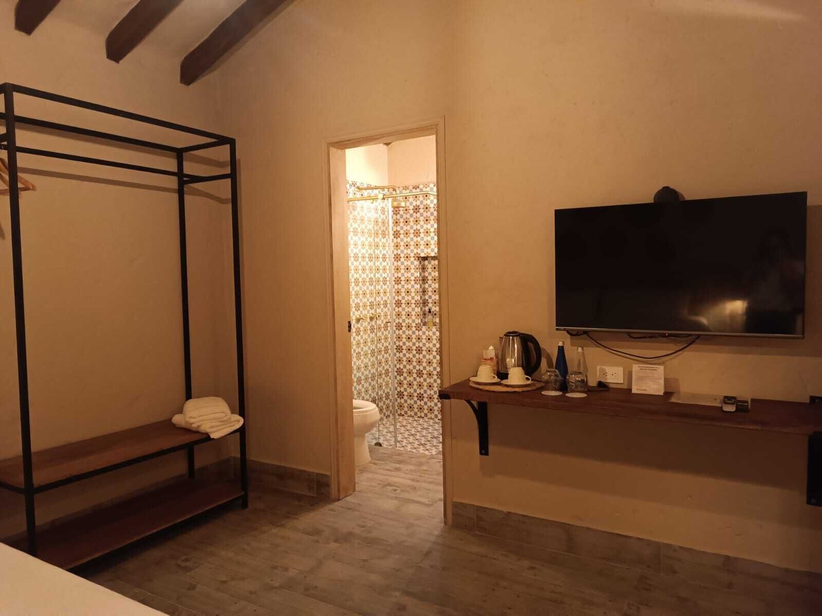 Una habitación con literas, un televisor, una mesita con una tetera y un baño visible a través de una puerta abierta.