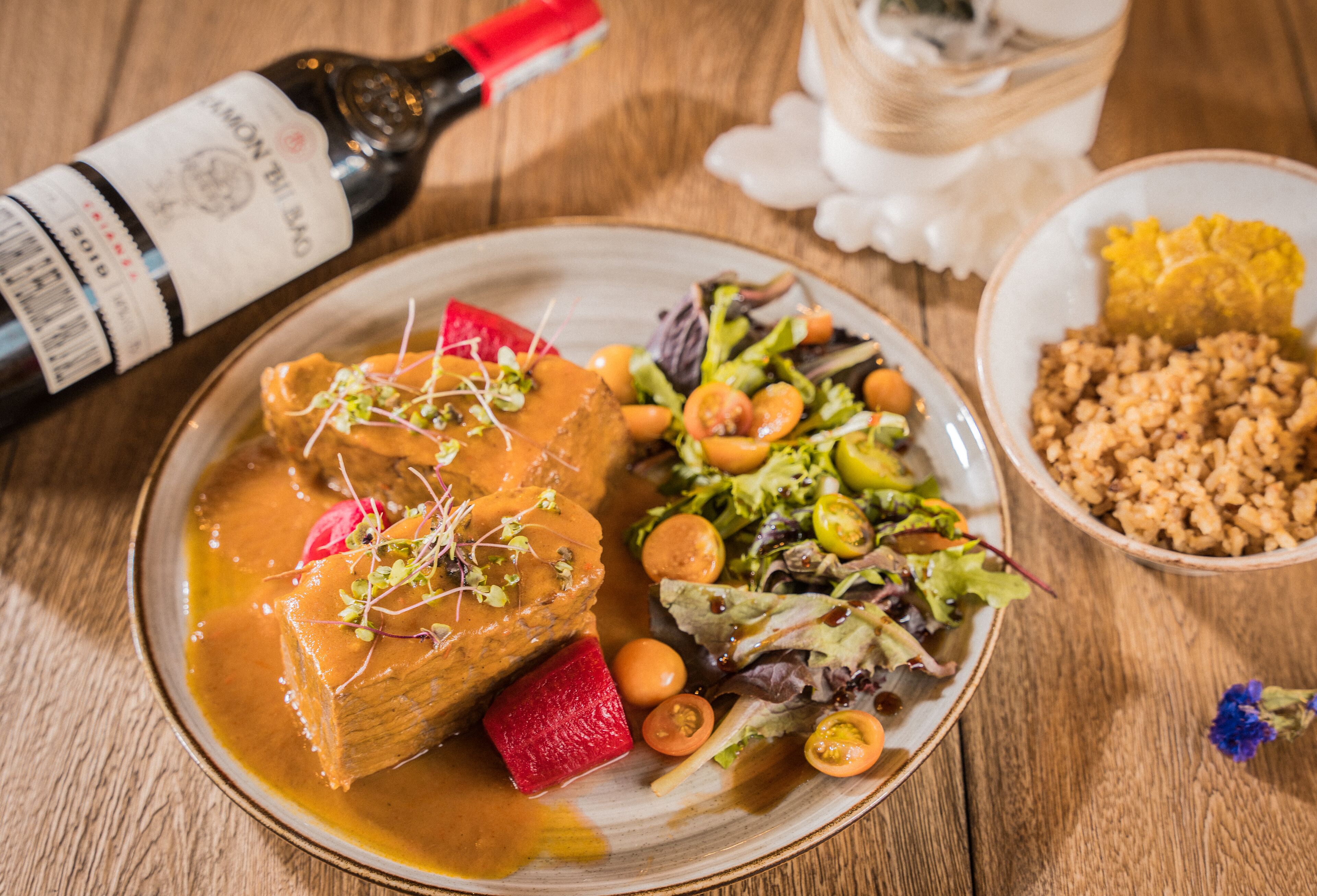 A plate of food with a bottle of wine and a glass on a wooden table.