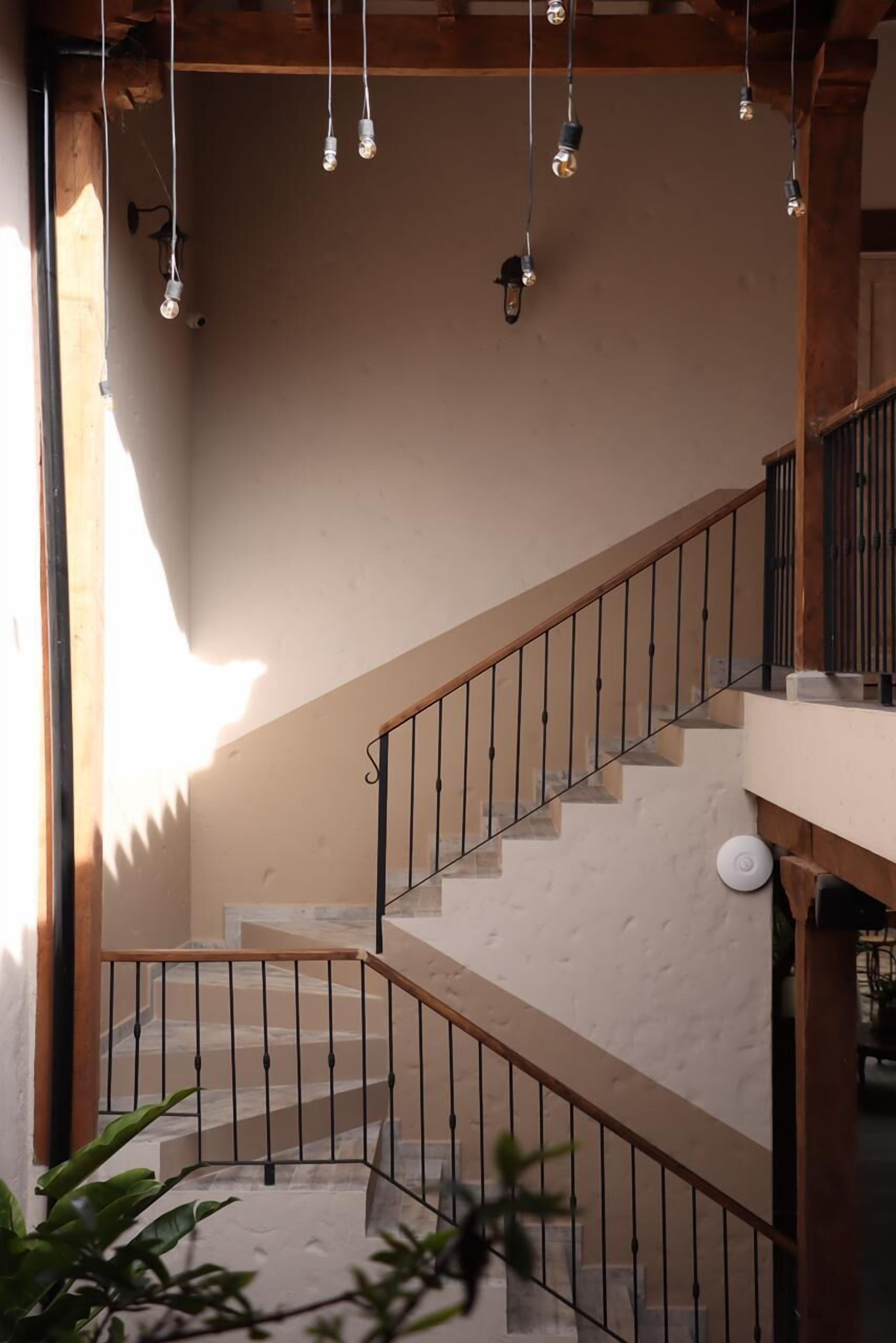Un escalier doté d’une main courante en bois et de balustrades en métal, menant à un palier avec un mur blanc et un luminaire suspendu.