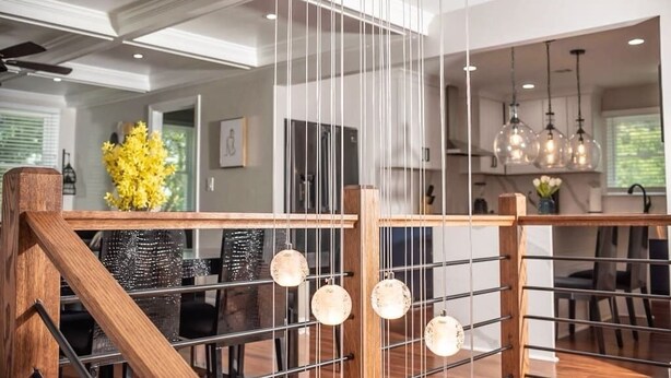 Ein modernes Interieur mit einer Holztreppe, einem Essbereich mit einer Chandelüster und einer Küche mit Pendelleuchten.