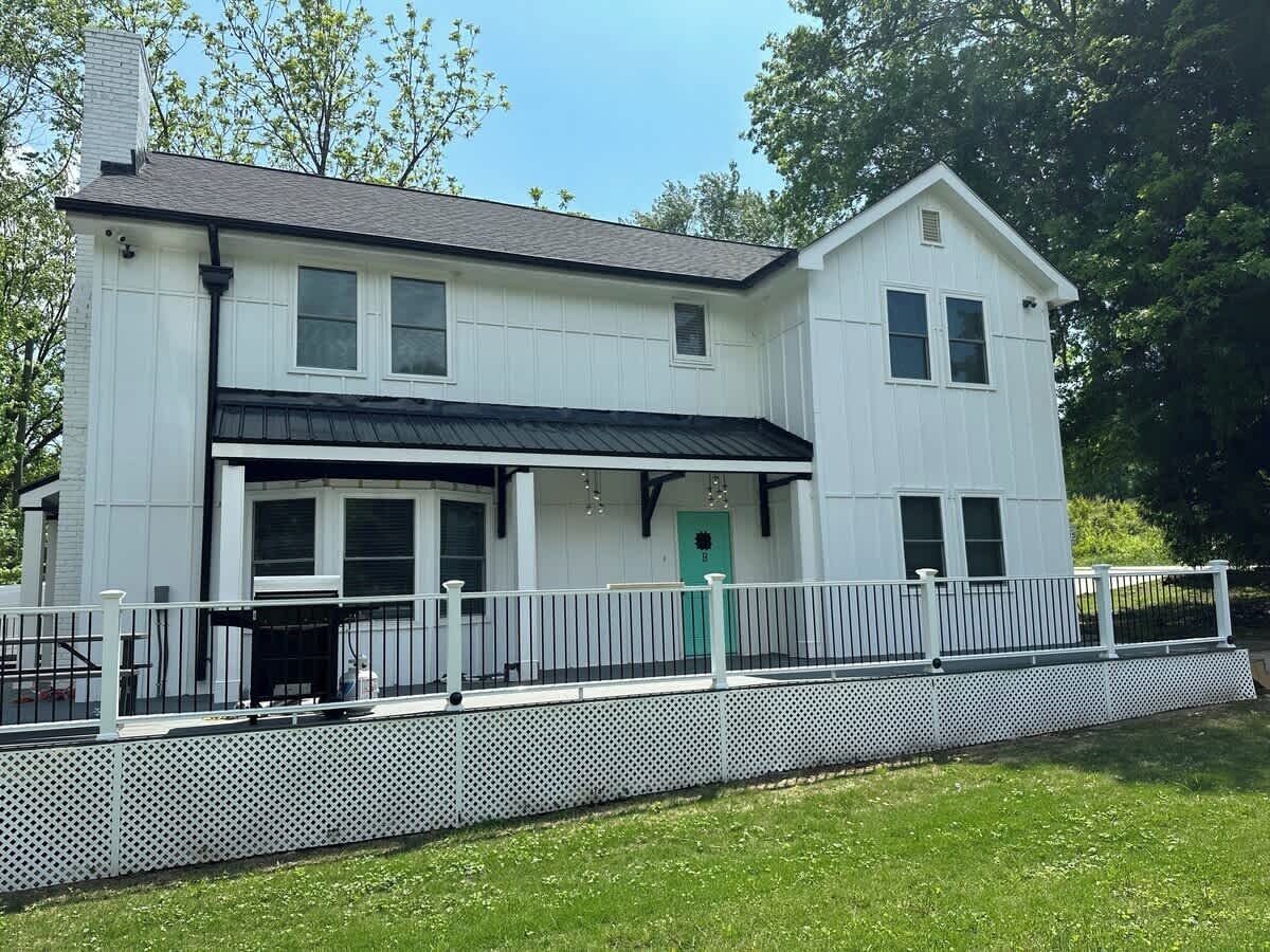 A two-story building with a porch, a green door, and a white fence.