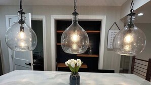 Ein Esstisch aus Marmor mit einer Vase voller weißer Blumen, drei hängenden Pendelleuchten und einer Tür im Hintergrund.
