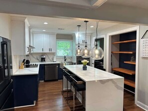 Una cocina moderna con armarios blancos, una isla central, luces colgantes y horno empotrado.