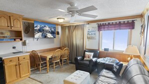 A compact living space with a dining area, a sofa, a ceiling fan, and a window with curtains. - ML390 King Bed Sleeps 8 Quiet Mountain View WiFi (Snowshoe)