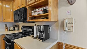 A kitchen with wooden cabinets, a black stove, a coffee maker, and a phone on the wall. - ML390 King Bed Sleeps 8 Quiet Mountain View WiFi (Snowshoe)