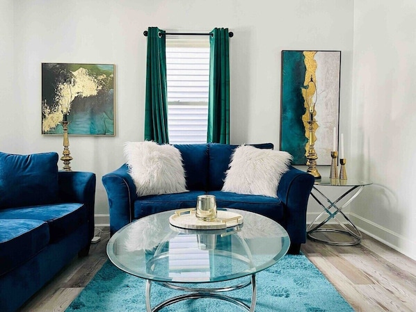 Un salon avec un canapé bleu, une table basse en verre et des œuvres d’art accrochées aux murs.