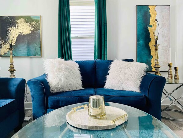 A modern living room with a blue sofa, white fluffy pillows, and a glass coffee table with a decorative item.