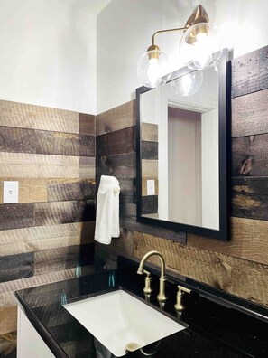 A bathroom with a black countertop sink, a white towel hanging on the wall, and a mirror with a black frame.