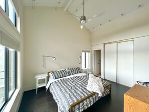 Een slaapkamer met een bed, nachtkastjes, een bureau, een plafondventilator en een garderobe.