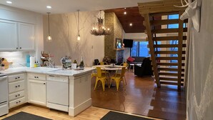 A modern kitchen with white cabinets, a central island, and a dining area with yellow chairs. - 100 FT to SLOPES! 4bd 3bth Ski-in ski- out Dobie Condo - walk to Mountain Inn (Wintergreen Resort)