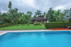 A swimming pool with a house in the background surrounded by lush greenery.