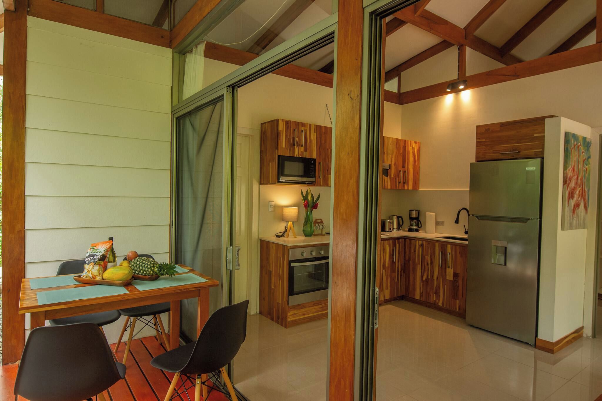 Cocina compacta con armarios de madera, refrigerador de acero inoxidable y comedor con mesa y sillas.