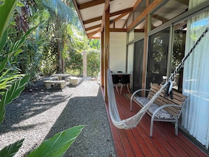 A covered outdoor seating area with a hammock, a table, and chairs.