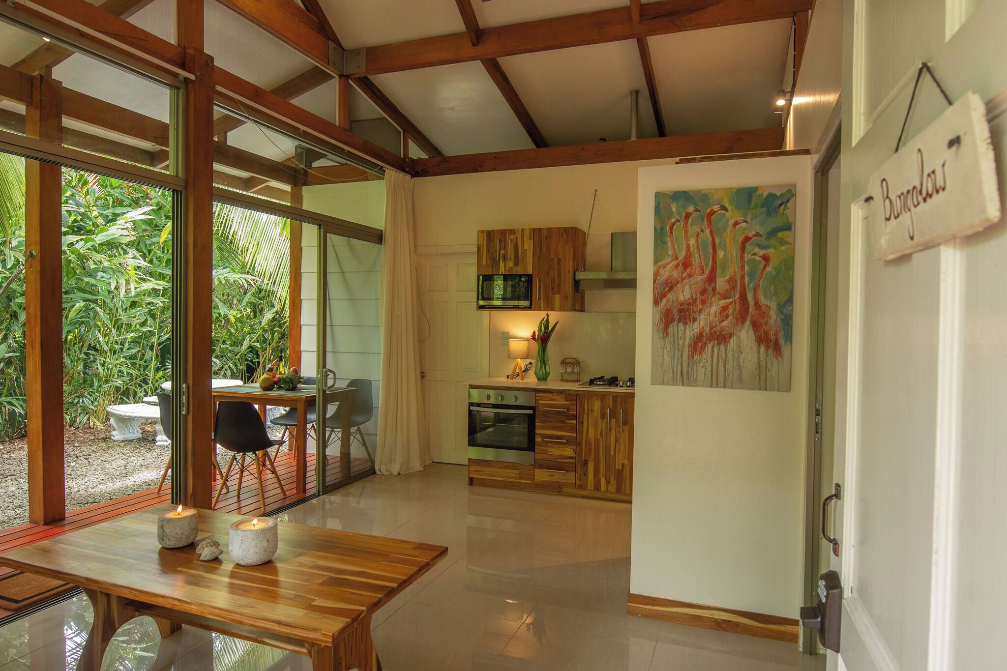 A modern kitchen with wooden cabinets, a dining area with a table and chairs, and a painting of flamingos on the wall.