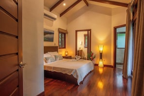 A bedroom with a bed, bedside lamps, a painting, and a view of the outdoors.