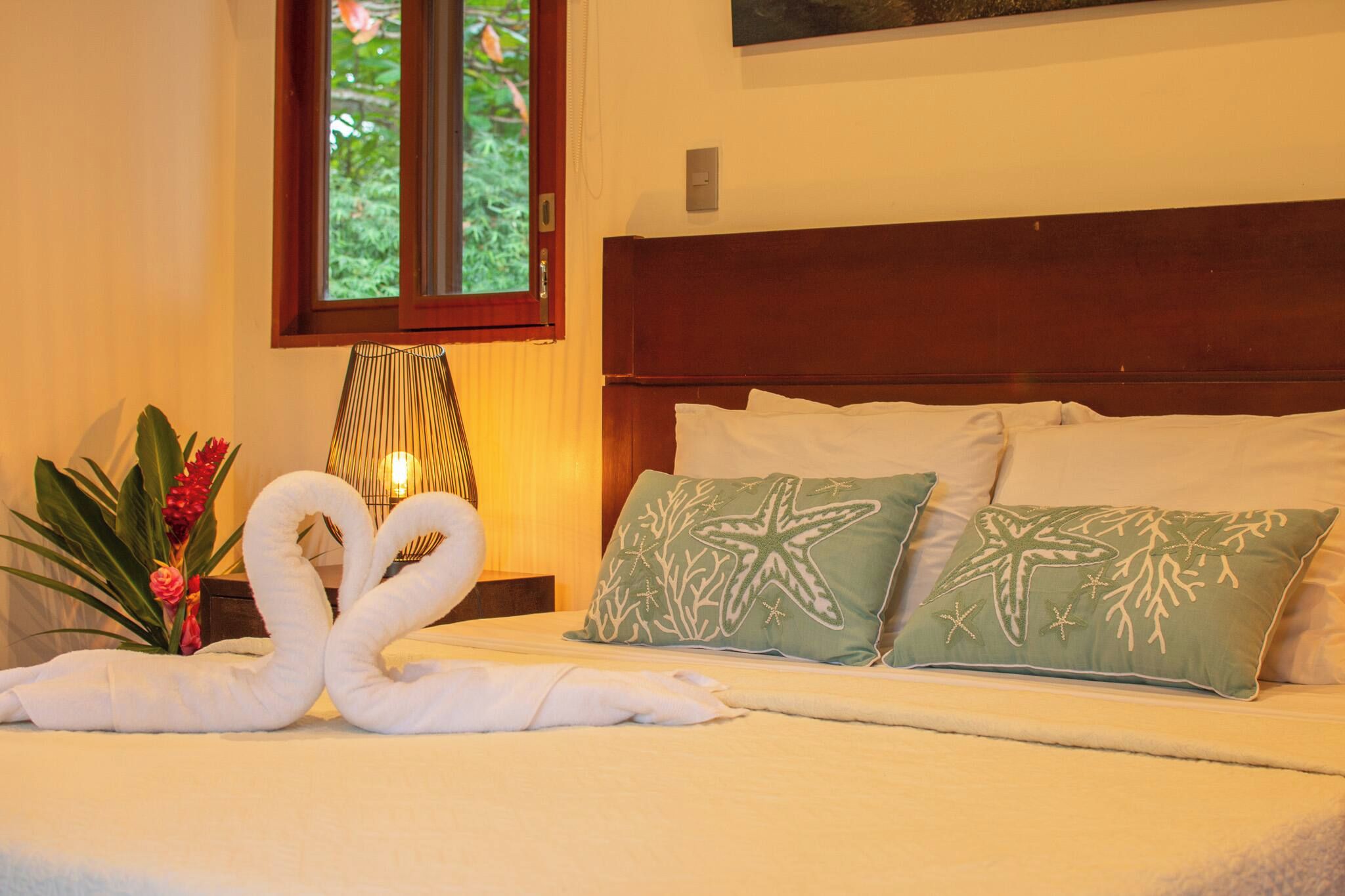 A hotel room with a bed, pillows, a lamp, and a plant.