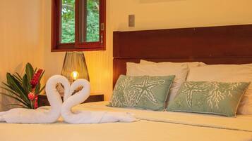 A hotel room with a bed, pillows, a lamp, and a plant.