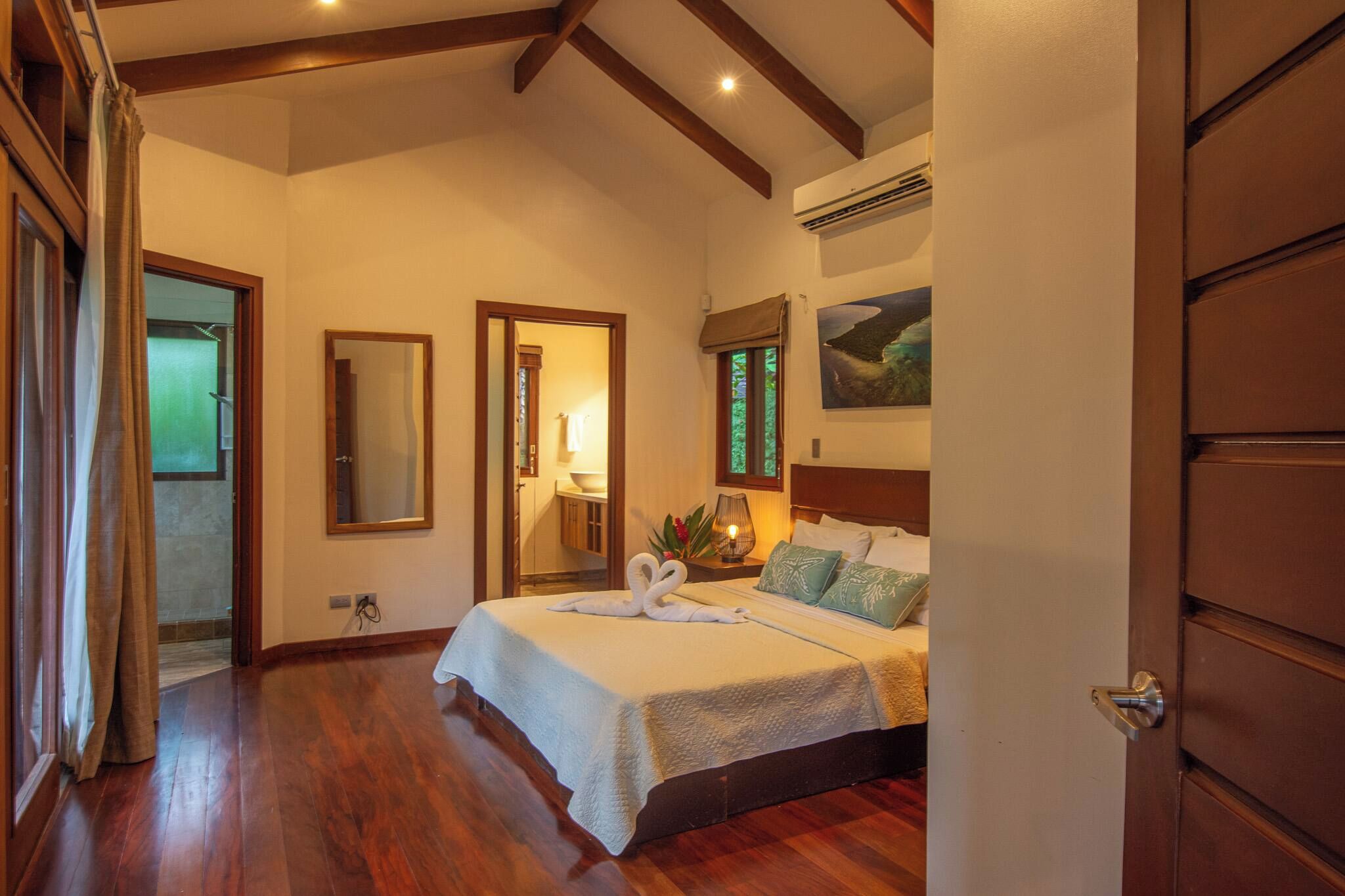 Un dormitorio con cama de madera, un espejo, una ventana con vistas y un equipo de aire acondicionado.