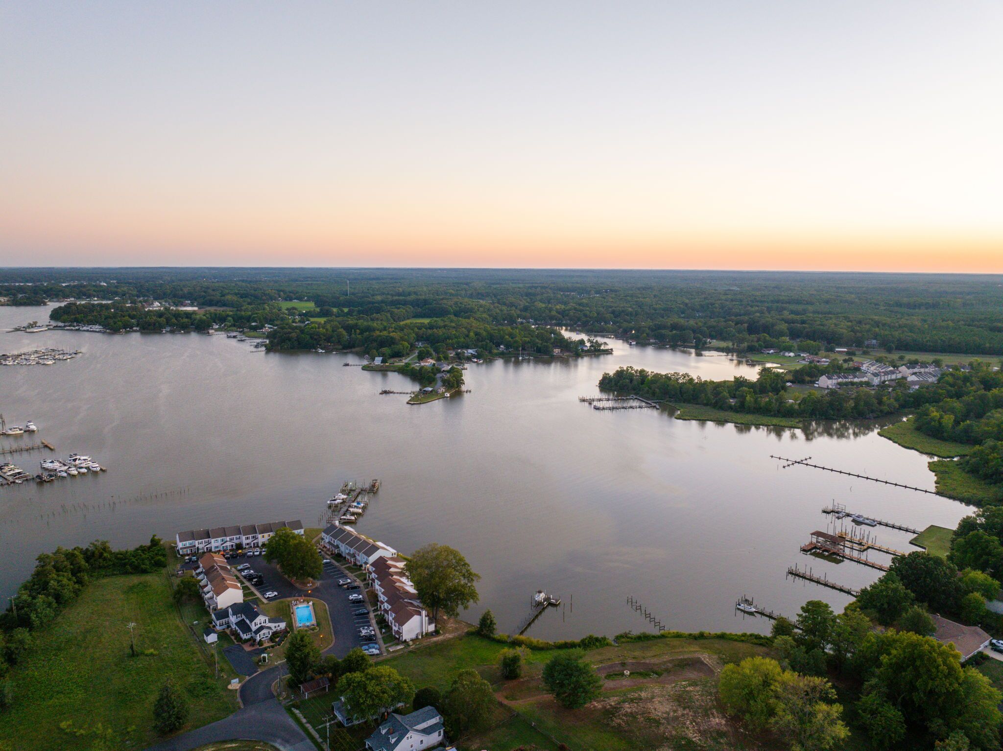 An aerial view of a lakeside property with a marina, multiple docks, and a row of white buildings with a swimming pool.