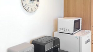 Une petite cuisine équipée d’un appareil à pain, d’un grille-pain, d’un four à micro-ondes et d’une horloge murale.