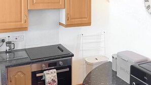 Une cuisine avec des meubles de rangement en bois, une cuisinière noire, un appareil à pain blanc et une bouilloire blanche.