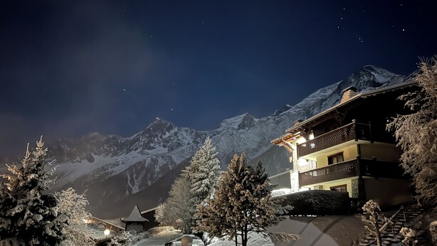 Eine verschneite Berglandschaft bei Nacht, mit einem Gebäude mit Balkonen und einem beleuchteten Innenraum.