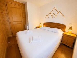 A neatly made bed with white linens and towels, a wooden headboard, and two bedside lamps. - Les Houches - Vacances à la Montagne (Les Houches)