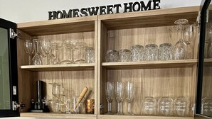 A wooden cabinet with shelves holding clear glassware and a sign that reads "HOMESWEET HOME".