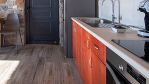 A kitchen with wooden cabinets, a stone wall, a black door, and a modern stove.