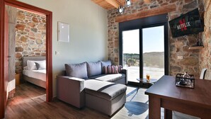 A cozy room with a stone wall, a bed, a sofa, a table, and a TV mounted on the wall.