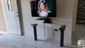 Ein Wohnzimmer mit einem an der Wand montierten Flachbildfernseher, einer Tür mit dekorativer Verkleidung und je einer hohen Vase mit Pflanzen auf beiden Seiten des Fernsehers.