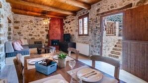 A stone-walled room with a wooden ceiling, a fireplace, a dining table set with plates, glasses, and a plant.