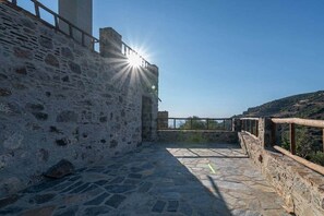 A stone courtyard with a wooden railing, a clear sky, and sunlight shining through.