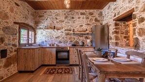 A rustic stone kitchen with wooden cabinetry, a built-in oven, and a dining area with a wooden table and chairs.