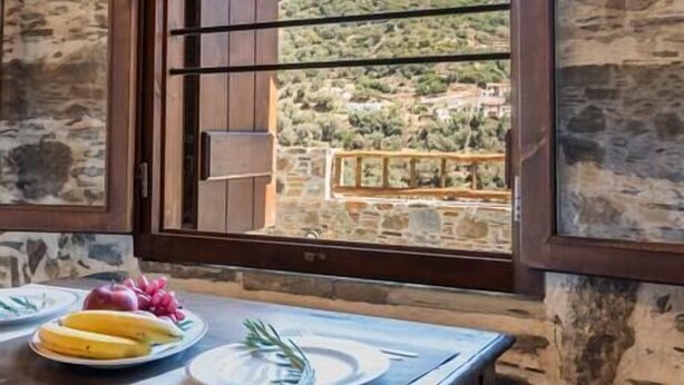 A stone wall with a wooden table and a window overlooking a hilly landscape.