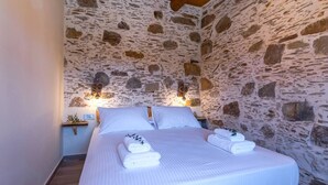 A bedroom with a stone wall, a wooden bed frame, and two bedside tables with lamps.
