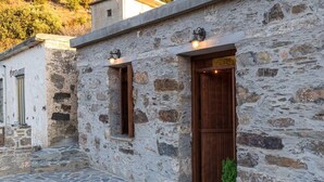 A stone building with a wooden door and windows, a potted plant, and a stone-paved courtyard.