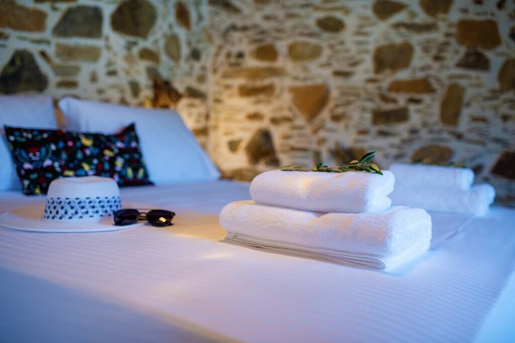 Un lit bien fait, avec des draps blancs, une serviette blanche pliée, un chapeau blanc et une paire de lunettes de soleil posées sur le lit.