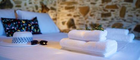 Un lit bien fait, avec des draps blancs, une serviette blanche pliée, un chapeau blanc et une paire de lunettes de soleil posées sur le lit.