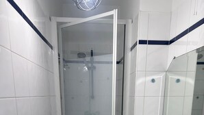 Et lille badeværelse med brusebad, vask og spejl.
