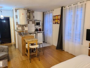 Une cuisine compacte équipée d’un four à micro-ondes, d’une cuisinière et d’un évier, une petite table en bois avec des chaises, et un lit dans la pièce adjacente.