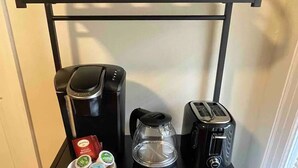Un coin cuisine équipé d’une machine à café, d’un grille-pain, d’une bouilloire et d’un four à micro-ondes, le tout installé sur un chariot en métal noir.