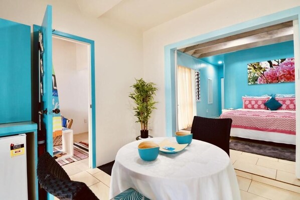 Ein Zimmer mit einem Bett, einem Tisch mit blauen Schüsseln, einem Stuhl und einer Zimmerpflanze.