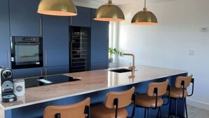 Una cucina moderna con isola centrale, sgabelli da bar, illuminazione a sospensione ed elettrodomestici integrati.