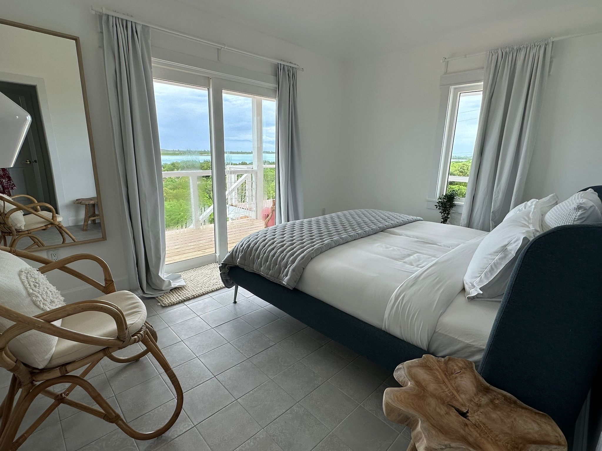 Ein Schlafzimmer mit Bett, Stuhl, Nachttisch aus Holz und einem Balkon mit Blick.