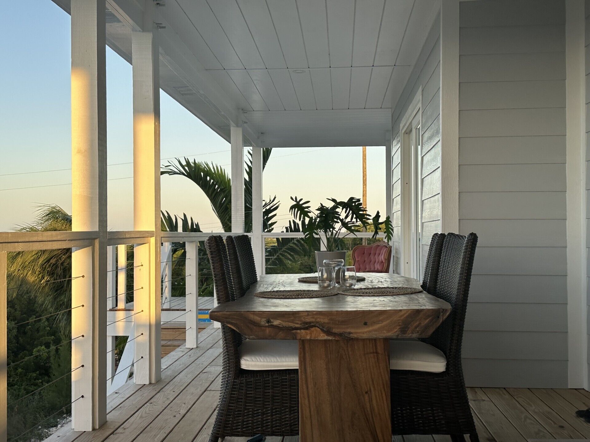 Un patio techado al aire libre con mesa y sillas, barandilla y vistas del paisaje circundante.
