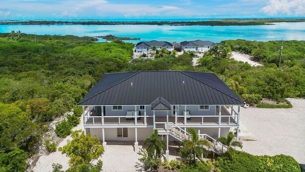 Una proprietà fronte spiaggia con una casa grande, un edificio più piccolo e una spiaggia sabbiosa.